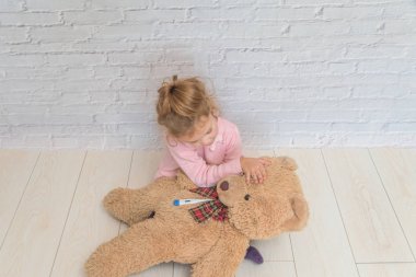 kız çocuk beyaz duvara karşı bir oyuncak ayının sıcaklık ölçer