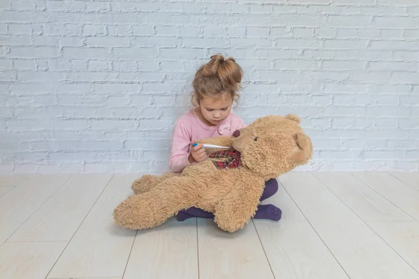Девочка Ребенок Измеряет Температуру Игрушечного Медведя Прислонившись Стене Белых Брикетов — стоковое фото