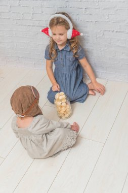 Kız, bir kavanoza bir pilotun kask ve Noel kulaklıklar, maskeli balo tatil çelenk ile katta oturan iki çocuk