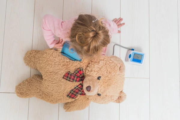 Una niña, un niño jugando médico, mide la presión de un oso — Foto de Stock