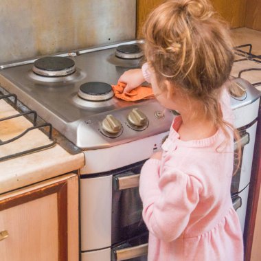 Kız çocuk, mutfakta yemek için soba yıkar.