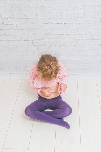 девочка делает инсулин выстрел в живот на фоне стенки белой брики
