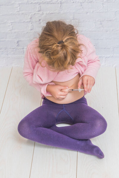 девочка делает инсулин выстрел в живот на фоне стенки белой брики
