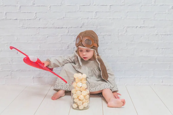 a girl, child in the helmet of the pilot with the aircraft and lights in the glass in front of a white brick wall