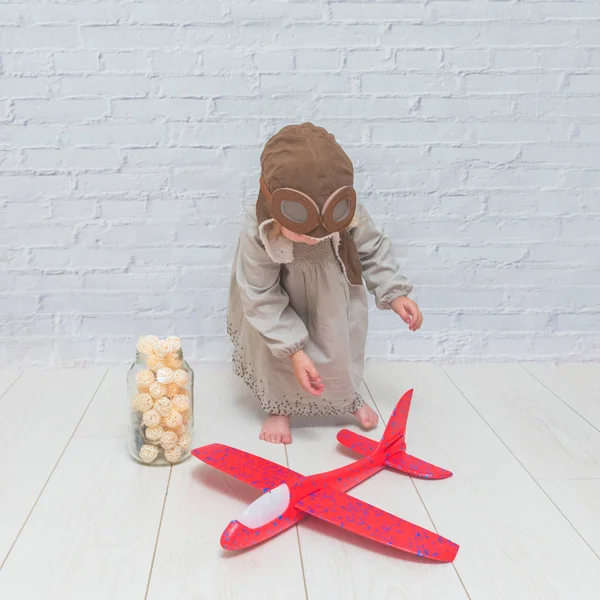 a girl, child in the helmet of the pilot with the aircraft and lights in the glass in front of a white brick wall