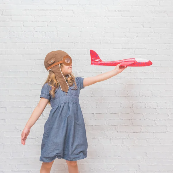 a girl, child in the helmet of the pilot with the aircraft and lights in the glass in front of a white brick wall