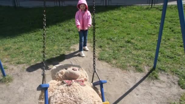 暖かい晴れた日、女の子、赤ちゃんがスイングおもちゃのクマに振る — ストック動画