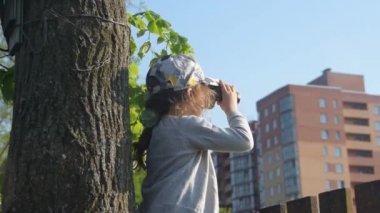 çitin üzerinde oturan çocuk dürbünden bakıyor.