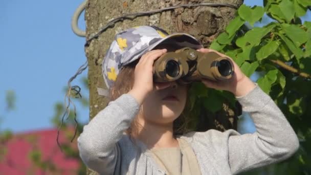 Das Kind, das auf dem Zaun sitzt und durch ein Fernglas schaut — Stockvideo