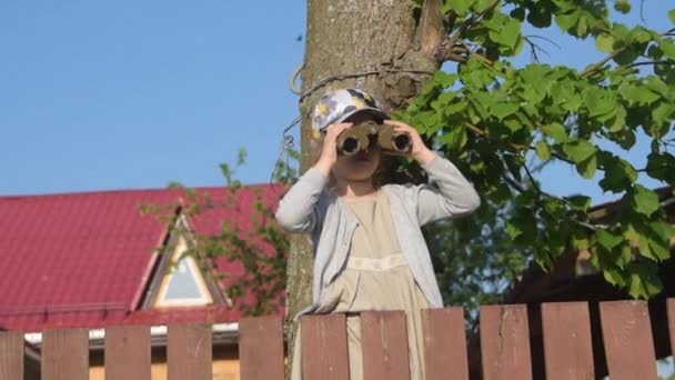 L'enfant assis sur la clôture regardant à travers les jumelles — Video