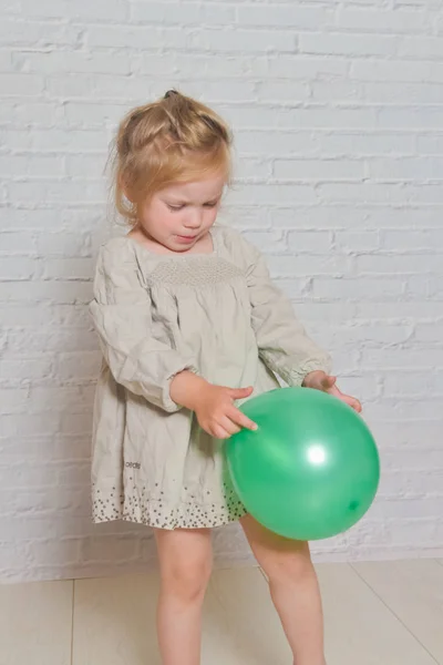 Yeşil bir balon ile beyaz bir tuğla duvar üzgün kız karşı — Stok fotoğraf