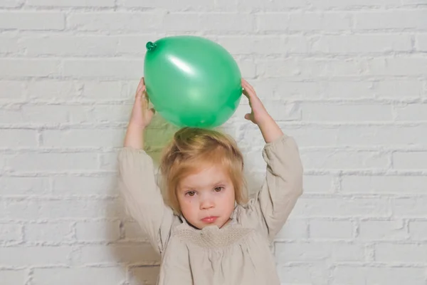 Contra una pared de ladrillo blanco chica triste con un globo verde — Foto de Stock