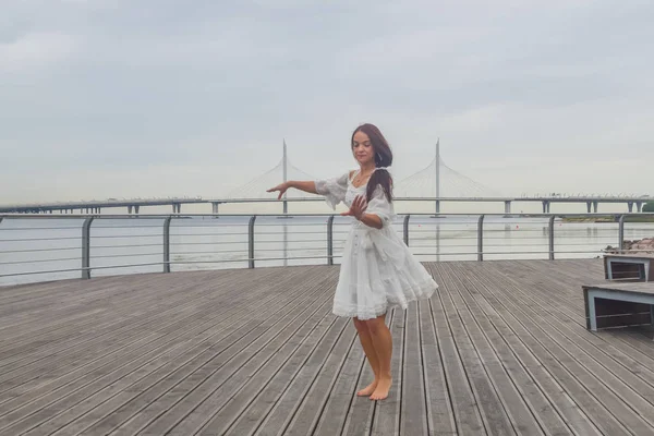 Dziewczyna na nabrzeżu w białej sukni taniec — Zdjęcie stockowe