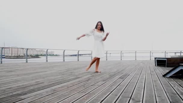 La chica frente al mar en un vestido blanco bailando — Vídeo de stock