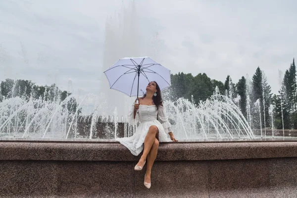Piękna dziewczyna w białej sukni i parasol przy fontannie na — Zdjęcie stockowe
