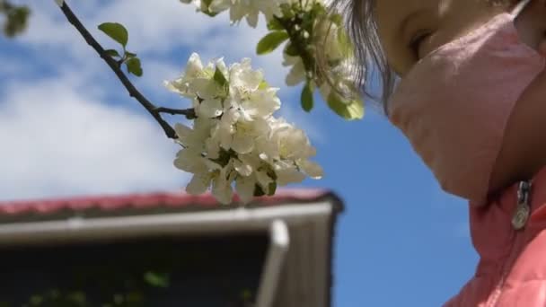 Ein Kind in Maske schnüffelt draußen Blumen — Stockvideo
