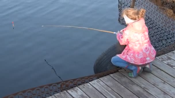Ett barn med fiskespö vid vattnet tittar på flottören — Stockvideo