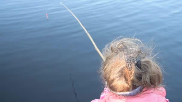 Ett barn med fiskespö vid vattnet tittar på flottören — Stockvideo