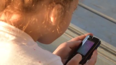 Bir kız çocuk dışarıda telefonla duygusal mesaj atıyor.