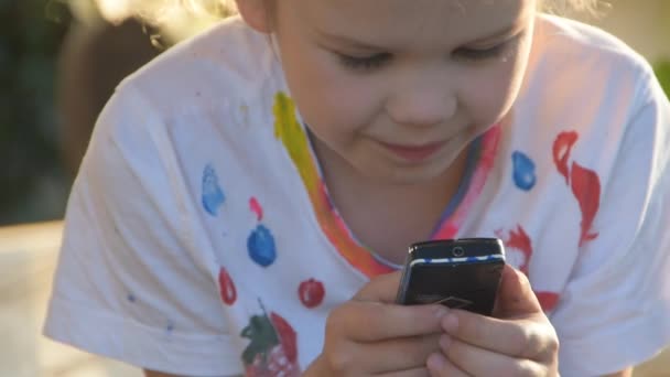 Uma menina criança está emocionalmente mensagens de texto no telefone fora — Vídeo de Stock