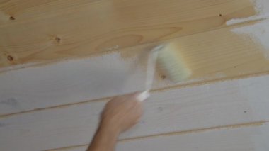 İşçinin eli ahşap bir duvarı beyaz boyalı bir fırçayla boyuyor.