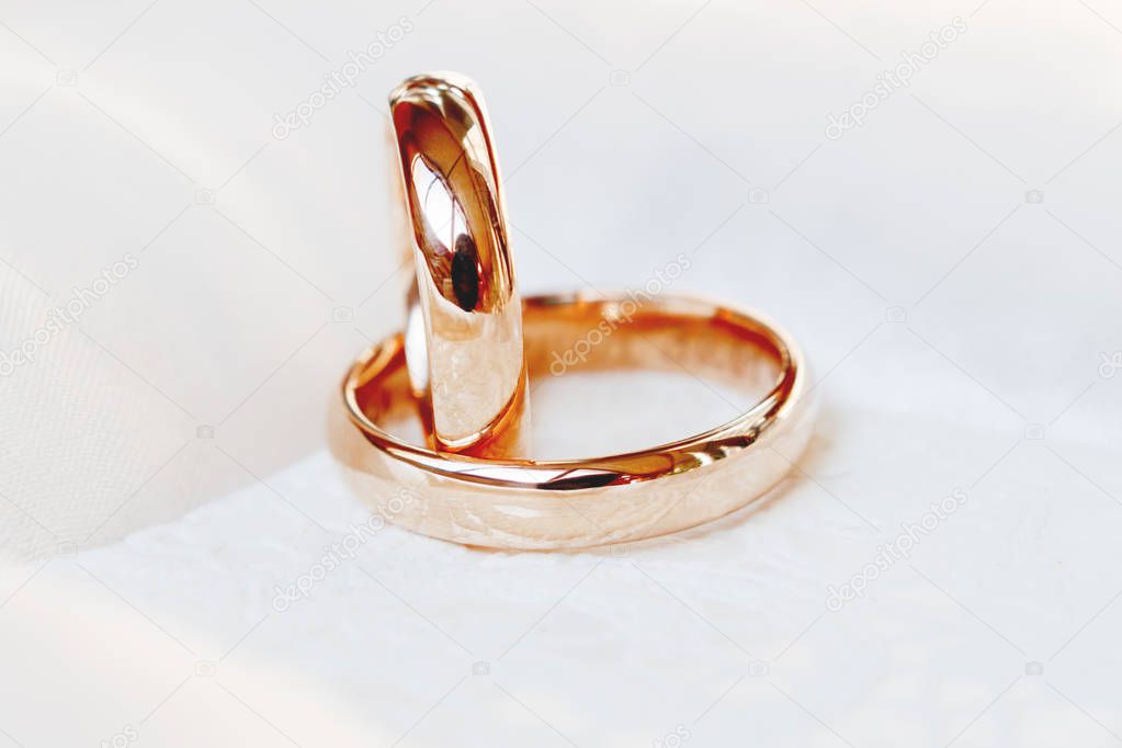 Golden wedding rings on white silk background. Wedding details. Symbol of love and marriage.