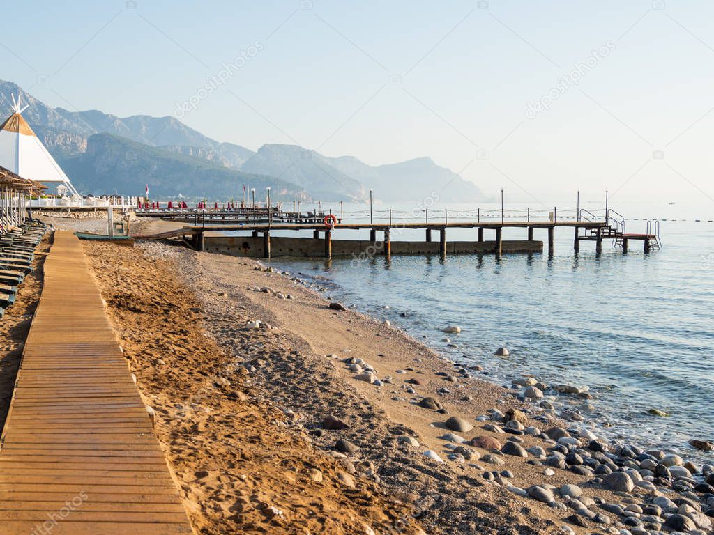 Early morning on the beach. Typical turkish hotel with sun loungers and wooden pontoon. Kemer, Turkey.