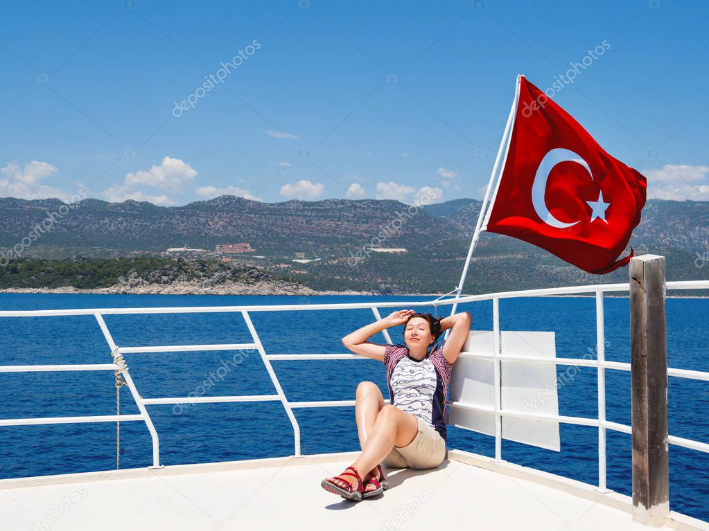 Tourist woman sunbathing on upper deck of yacht. Red flag on Turkey. On the way to famous Kekova island.