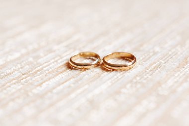 Bej kumaş zemin üzerine altın alyans. Düğün detayları, sevgi ve evlilik sembolü.