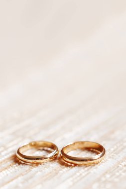 Bej kumaş zemin üzerine altın alyans. Düğün detayları, sevgi ve evlilik sembolü. Metin için yer.