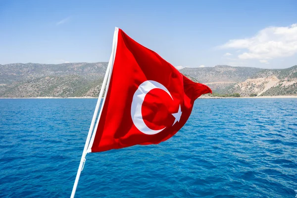 Flag of Turkey waving in the wind against Mediterranean sea in sunny day.