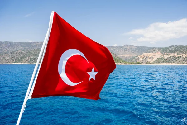 Flag of Turkey waving in the wind against Mediterranean sea in sunny day.