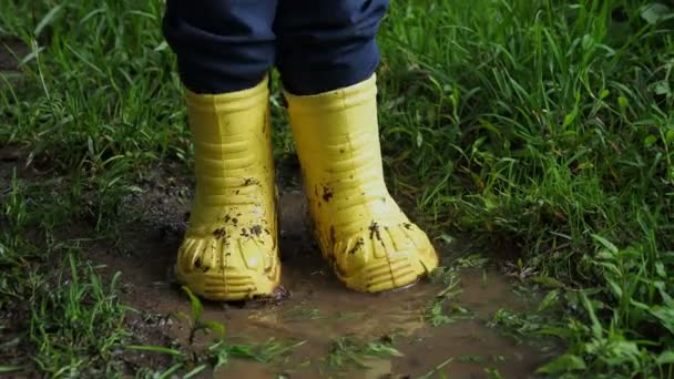 小孩子在明亮的黄色橡胶靴子溅在水坑 儿童脚保护不受污染的水 — 图库视频影像