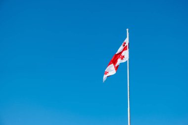 Rüzgara karşı açık mavi gökyüzü güneşli bir günde sallayarak Gürcistan bayrağı.