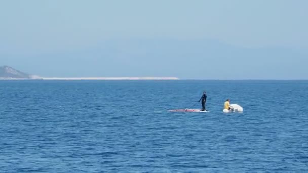 DEMRE, TURQUIA - 16 de maio de 2018. A mulher de fato de mergulho está a levantar a vela do windsurf da água. Homem no barco inflável com motor está flutuando perto dela. Turquia . — Vídeo de Stock
