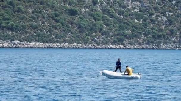 DEMRE, TURQUÍA - 16 de mayo de 2018. Mujer en traje de neopreno está levantando la vela de windsurf fuera del agua. El hombre en barco inflable con motor flota cerca de ella. Turquía . — Vídeos de Stock