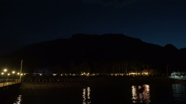 Vista nocturna en la playa con tumbonas, montañas y estrellas . — Vídeos de Stock