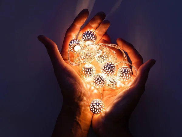 Hands with light bulbs. Metal light bulbs with delicate pattern shine in dark. Holiday decoration with magic light reflections.