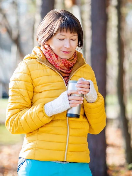 Parlak sarı ceketli mutlu geniş gülümseyen kadın Termos Kupa tutarak. Sıcak çay veya diğer içecek serin sonbahar günü.