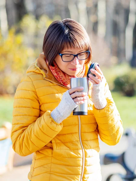 Parlak sarı ceketli mutlu geniş gülümseyen kadın Termos Kupa tutarak. Sıcak çay veya diğer içecek serin sonbahar günü.