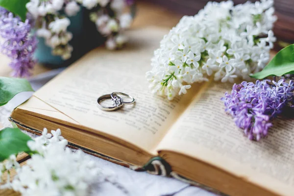 Pair of wedding rings with diamond. Rustic background with old books and lilac flowers. Retro background.