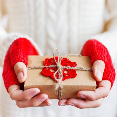 Kadın beyaz örgü kazak ve hediye tutan ellere Kraft kağıt dantelli kırmızı kar tanesi ile paketlenmiş. DIY Noel ve yeni yıl, St Sevgililer günü hediyesi.
