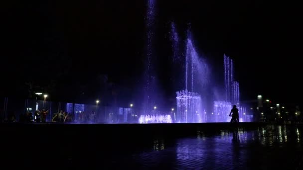 Adler, Rusland -, 9 oktober 2018. Toeristen schieten van de zingende fontein met smartphones. Man met kind is het berijden van een fiets. — Stockvideo