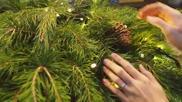 Mujer acaricia corona de Navidad hecha de ramas de pino con conos de pino y bombillas. Fondo de Año Nuevo . — Vídeos de Stock