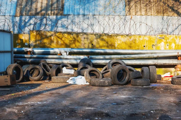 Los neumáticos viejos del coche se apilan contra una cerca con alambre de púas. Contaminación ambiental . — Foto de Stock