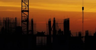Konut bina inşaatı. İnşaatçılar bağlantı parçaları çıkıntılı bitmemiş yere gidin. Arka planda bir turuncu günbatımı işçilerin siluetleri.