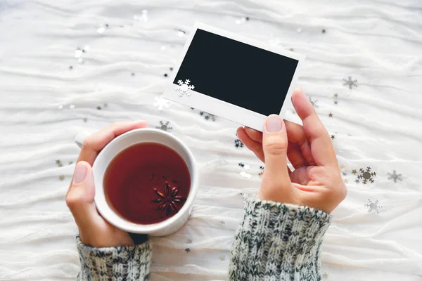 Vrouw houdt een kopje thee en foto. Winter weefsel achtergrond met mousserende zilveren sneeuwvlokken. Leeg fotokader voor uw tekst of afbeelding. — Stockfoto