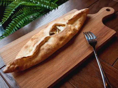 Mozzarella peyniri, kaşar peyniri ve istiridye mantar ile bir tekne şeklinde pişmiş bun. Ahşap doğrama tahtası üzerinde pasta.