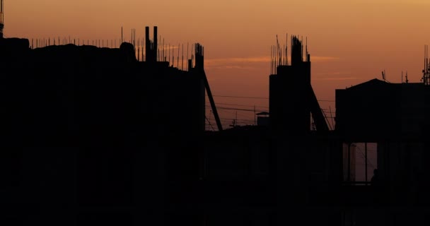 Budowa budynku mieszkalnego. Budowniczych przejdź na dnie niedokończone z wystające okucia. Sylwetki pracowników na tle pomarańczowy zachód słońca. — Wideo stockowe