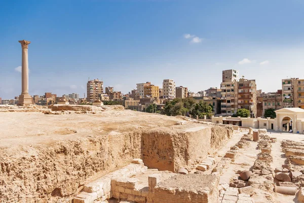 O Pilar de Pompeu, coluna triunfal romana, com duas estátuas de Esfinge localizadas no Serapeu de Alexandria. Marco arquitetônico antigo no Egito . — Fotografia de Stock